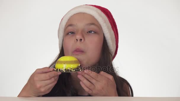 食欲と白い背景ストック映像ビデオで誕生日ケーキを食べる喜びとサンタ クロースの帽子の美しい十代の少女 — ストック動画