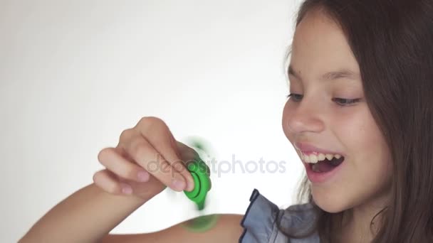 Bela menina adolescente alegre jogando com fidget spinner verde no fundo branco imagens de vídeo — Vídeo de Stock