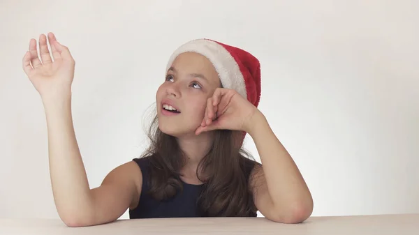 Hermosa chica feliz adolescente en un Santa Claus sombrero mirada y emocionalmente expresa una sorpresa sobre fondo blanco — Foto de Stock