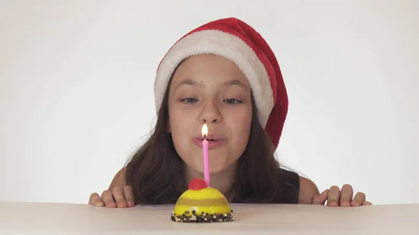 Hermosa chica traviesa adolescente en un sombrero de Santa Claus sopla una vela en un pastel festivo sobre fondo blanco — Foto de Stock