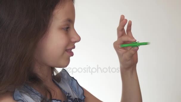 Bela menina adolescente alegre jogando com fidget spinner verde no fundo branco imagens de vídeo — Vídeo de Stock