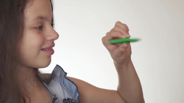 Bela menina adolescente alegre jogando com fidget spinner verde no fundo branco imagens de vídeo — Vídeo de Stock