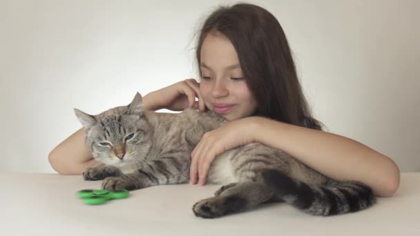 Hermosa chica adolescente alegre con un gato jugando con verde fidget spinner sobre fondo blanco archivo de vídeo — Vídeo de stock