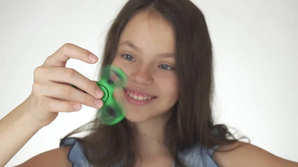 Веселая девочка-подросток, играющая с зеленым фиолетовым спиннером на белом фоне — стоковое фото