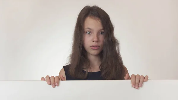 Krásná dívka dospívající držení plakát s informacemi a je překvapen, na bílém pozadí — Stock fotografie