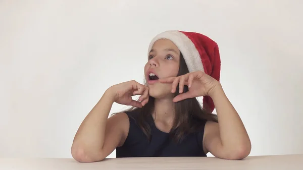 Menina feliz bonita adolescente em um olhar de chapéu de Papai Noel e emocionalmente expressa uma surpresa no fundo branco — Fotografia de Stock