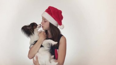 Bir Noel Baba şapkası ve sevinçle öpüşme ve beyaz arka plan stok görüntüleri video dalga geçmeyi köpek kıta oyuncak İspanyol Papillon güzel genç kız.