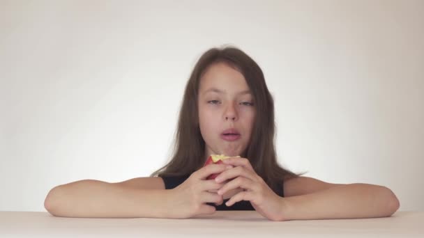 Beautiful happy teenage girl with appetite and pleasure eating red fresh delicious apple on white background footage video — стоковое видео