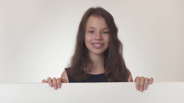 Piękna dziewczyna nastolatek patrzy na plakat z informacjami i radośnie reklamuje go na białym tle Stockowy wideo. — Wideo stockowe