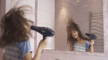 Güzel mutlu kız genç saç kurutma makinesi ile saç kurur ve şarkı söyler ve banyoda bir ayna önünde dans ediyor