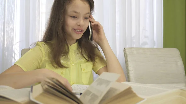 Adolescente menina é distraída por conversa telefônica ao fazer seu dever de casa — Fotografia de Stock