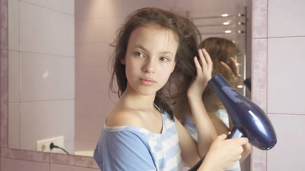 Красива дівчина-підліток сушить волосся фен у ванній — стокове фото