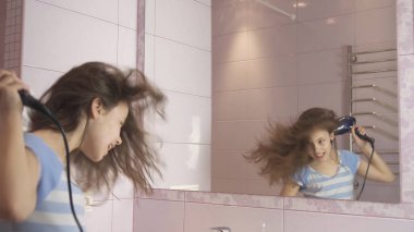 Güzel mutlu kız genç saç kurutma makinesi ile saç kurur ve şarkı söyler ve banyoda bir ayna önünde dans ediyor