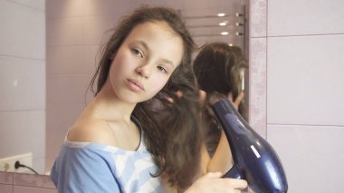 Güzel genç kız saç banyoda bir saç kurutma makinesi kurur.