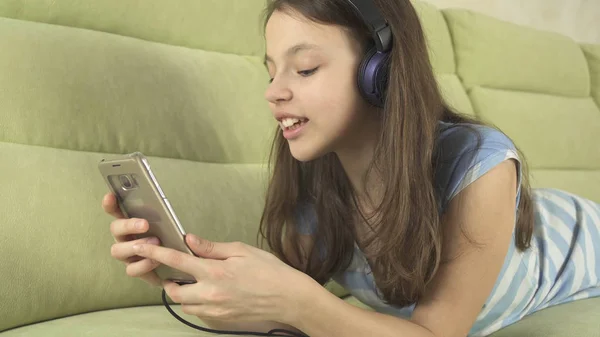 Beautiful teen girl in headphones singing karaoke songs in smartphone — Stock Photo, Image