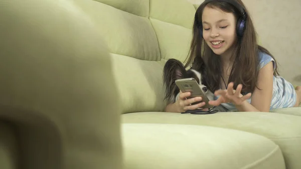 Vacker tonåring flicka i hörlurar sjunger karaokelåtar i smartphone med hund — Stockfoto
