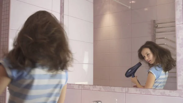 Hermosa chica feliz adolescente seca el cabello con secador de pelo y canta y baila delante de un espejo en el baño — Foto de Stock