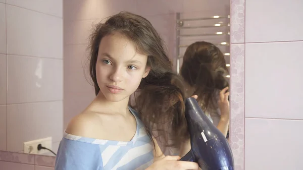 Hermosa chica adolescente seca el cabello un secador de pelo en el baño — Foto de Stock