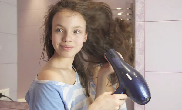 Όμορφη έφηβος κορίτσι στεγνώνει τα μαλλιά στεγνωτήρα μαλλιών στο μπάνιο — Φωτογραφία Αρχείου