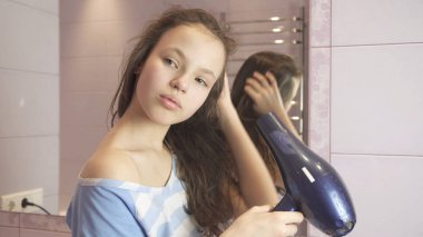 Güzel genç kız saç banyoda bir saç kurutma makinesi kurur.