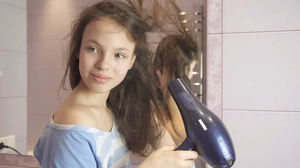 Beautiful teen girl dries hair a hairdryer in bathroom — Stock Photo, Image