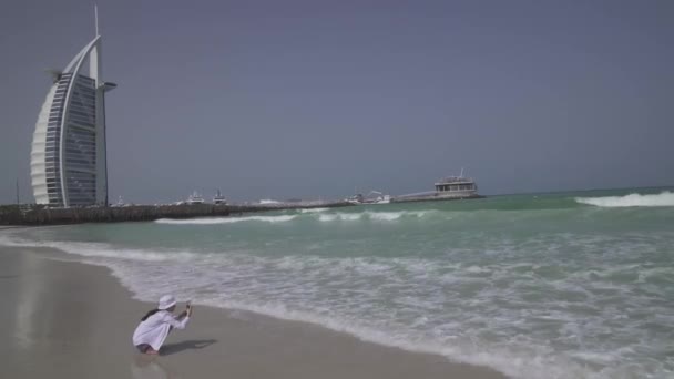 Teenage girl takes pictures of the sea waves on Public Jumeirah Open Beach on the coast of the Persian Gulf, Dubai stock footage video — Stock Video