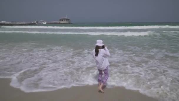 Teenage girl takes pictures of the sea waves of the Persian Gulf on smartphone on the beach of Dubai stock footage video — Stock Video