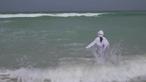 Adolescente em roupas alegremente pulando nas ondas do Golfo Pérsico na praia de Dubai vídeo de imagens — Vídeo de Stock