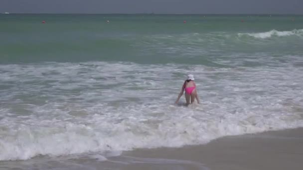 Adolescente en un traje de baño salta felizmente en las olas del Golfo Pérsico en la playa de Dubai material de archivo de vídeo — Vídeos de Stock