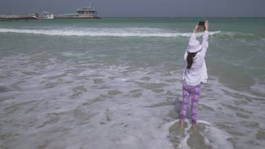Genç kız Basra Körfezi'nin dalgalar deniz smartphone cep telefonu ile Dubai beach stok görüntüleri üzerinde video çekiyor