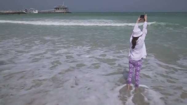 Adolescente toma fotos de las olas del mar del Golfo Pérsico en el teléfono inteligente en la playa de Dubai archivo de vídeo — Vídeos de Stock