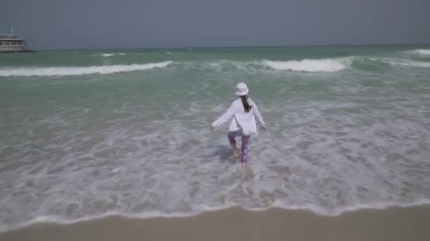 Adolescente in abiti gioiosamente saltando tra le onde del Golfo Persico sulla spiaggia di Dubai stock footage video — Video Stock