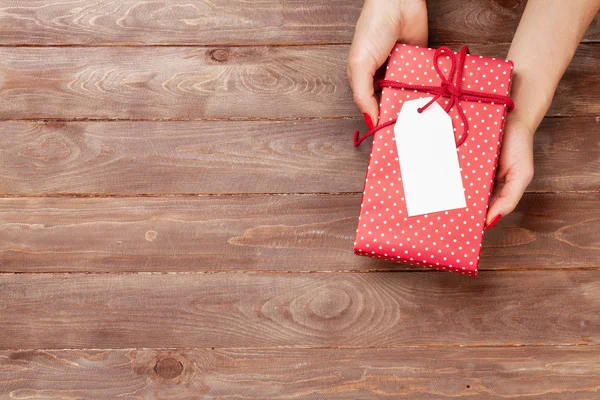 Mani femminili che tengono il regalo sopra il tavolo di legno — Foto Stock