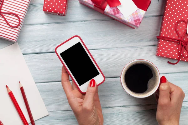 Mujer sosteniendo smartphone y envolviendo regalos — Foto de Stock