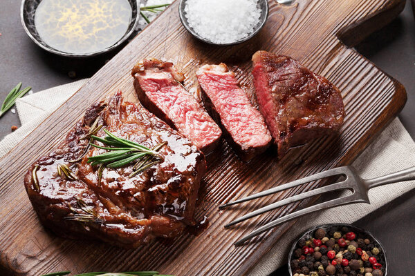 Grilled ribeye beef steak, herbs and spices on cutting board