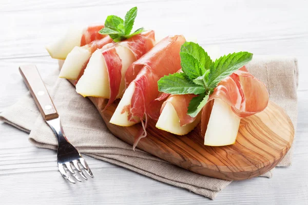 鲜瓜与意大利熏火腿和薄荷木制的桌子上 — 图库照片