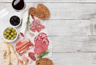 Salam, dilimlenmiş jambon, sosis, jambon, pastırma, tost, zeytin. Et meze tabağı ve ahşap masa üzerinde kırmızı şarap. Kopya alanı ile Üstten Görünüm