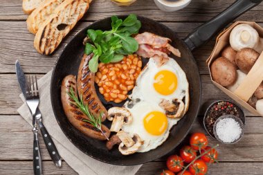 Kızarmış yumurta, sosis, pastırma, fasulye, tost, domates, portakal suyu ve kahve fincanı ahşap masa üzerinde. Üstten Görünüm