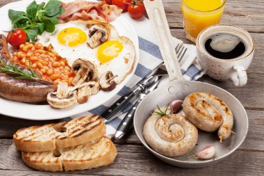 Kızarmış yumurta, sosis, pastırma, fasulye, tost, domates, portakal suyu ve kahve fincanı ahşap masa üzerinde. Üstten Görünüm