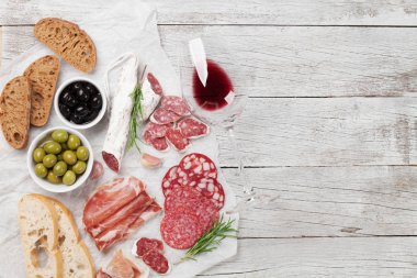Salam, dilimlenmiş jambon, sosis, jambon, pastırma, tost, zeytin. Et meze tabağı ve ahşap masa üzerinde kırmızı şarap. Kopya alanı ile Üstten Görünüm