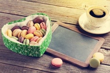 Renkli macaroons Sevgililer günü kalp şeklinde hediye kutusu ve kahve Kupası tahta masada. Kara tahta ile selam için