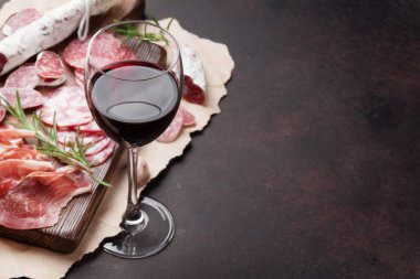 Salam, jambon, sosis, jambon, pastırma ve kırmızı şarap cam dilimlenmiş. Et meze tabağı taş masada. Kopya alanı ile
