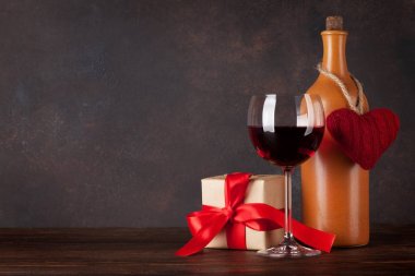 Sevgililer günü tebrik kartı ile kırmızı şarap şişesi, kara tahta önünde ahşap masa üzerinde kalp oyuncak ve hediye kutusu.