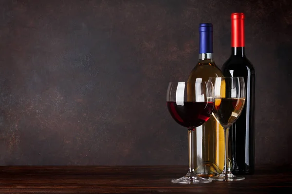 Red and white wine bottles and glasses in front of blackboard wall. With copy space