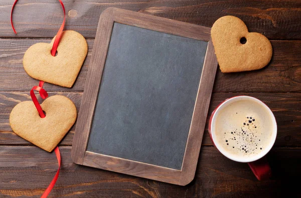 Valentines day greeting card with heart cookies and coffee cup on wooden table. With chalkboard