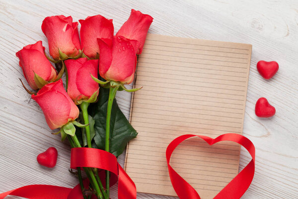 Valentines day greeting card with red roses and heart shaped ribbon on wooden background. Top view with space 