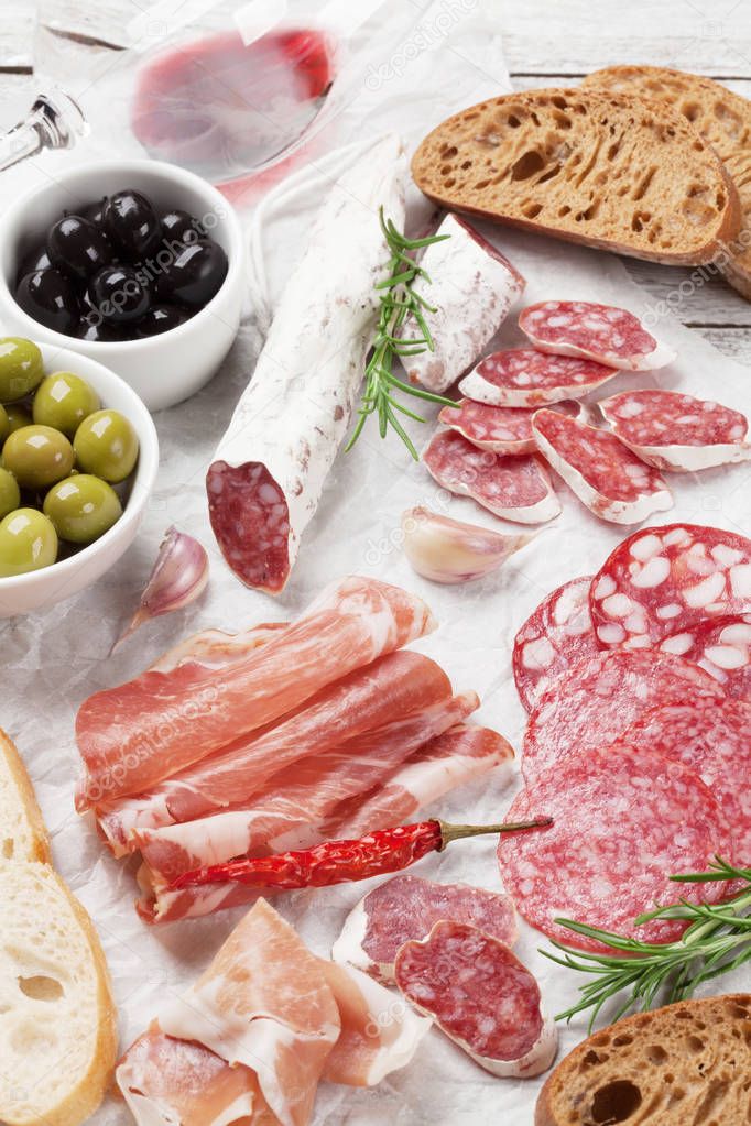 Salami, sliced ham, sausage, prosciutto, bacon, toasts, olives. Meat antipasto platter and red wine on wooden table