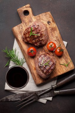Grilled fillet steaks on cutting board and glass of red wine. Top view clipart