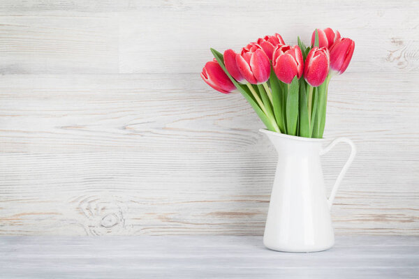 Red tulips bouquet in pitcher in front of wooden wall.  Easter greeting card with space for your greetings