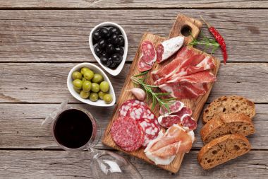 Salam, dilimlenmiş jambon, sosis, jambon, pastırma, tost, zeytin. Et meze tabağı ve ahşap masa üzerinde kırmızı şarap. Kopya alanı ile Üstten Görünüm